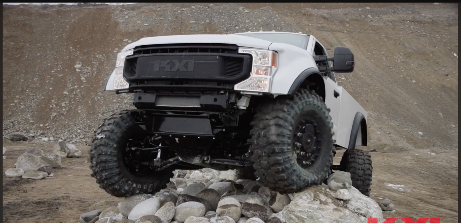 A white KXI Wildertec truck with enormous tyres climbing a pile of boulders